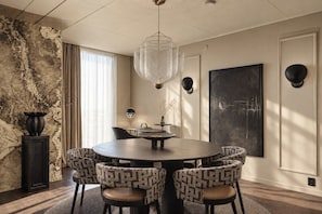Ein modernes Esszimmer mit einem runden Tisch, gemusterten Stühlen, einer Hängelampe und einem großen abstrakten Gemälde an der Wand.