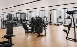 Ein Fitnessraum mit unterschiedlichen Trainingsgeräten, großen Fenstern und Holzboden.