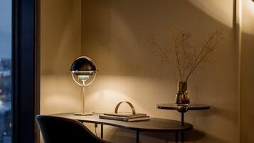 A modern interior with a dining area featuring a round table, a chair, a lamp, and a vase with branches.