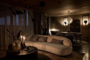 Ein modernes Wohnzimmer mit einer Couch, einem Couchtisch und einer dekorativen Vase. Es gibt einen Essbereich mit einer Kronleuchter und gemusterten Stühlen.