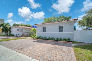 A residential property with a paved driveway, a small front yard with plants, and a clear blue sky. - The 280 House | Newly Renovated Near Miami Airport (Miami)