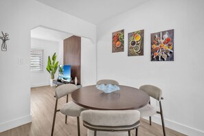 A modern dining area with a round table, four chairs, and three wall-mounted artworks. - The 280 House | Newly Renovated Near Miami Airport (Miami)