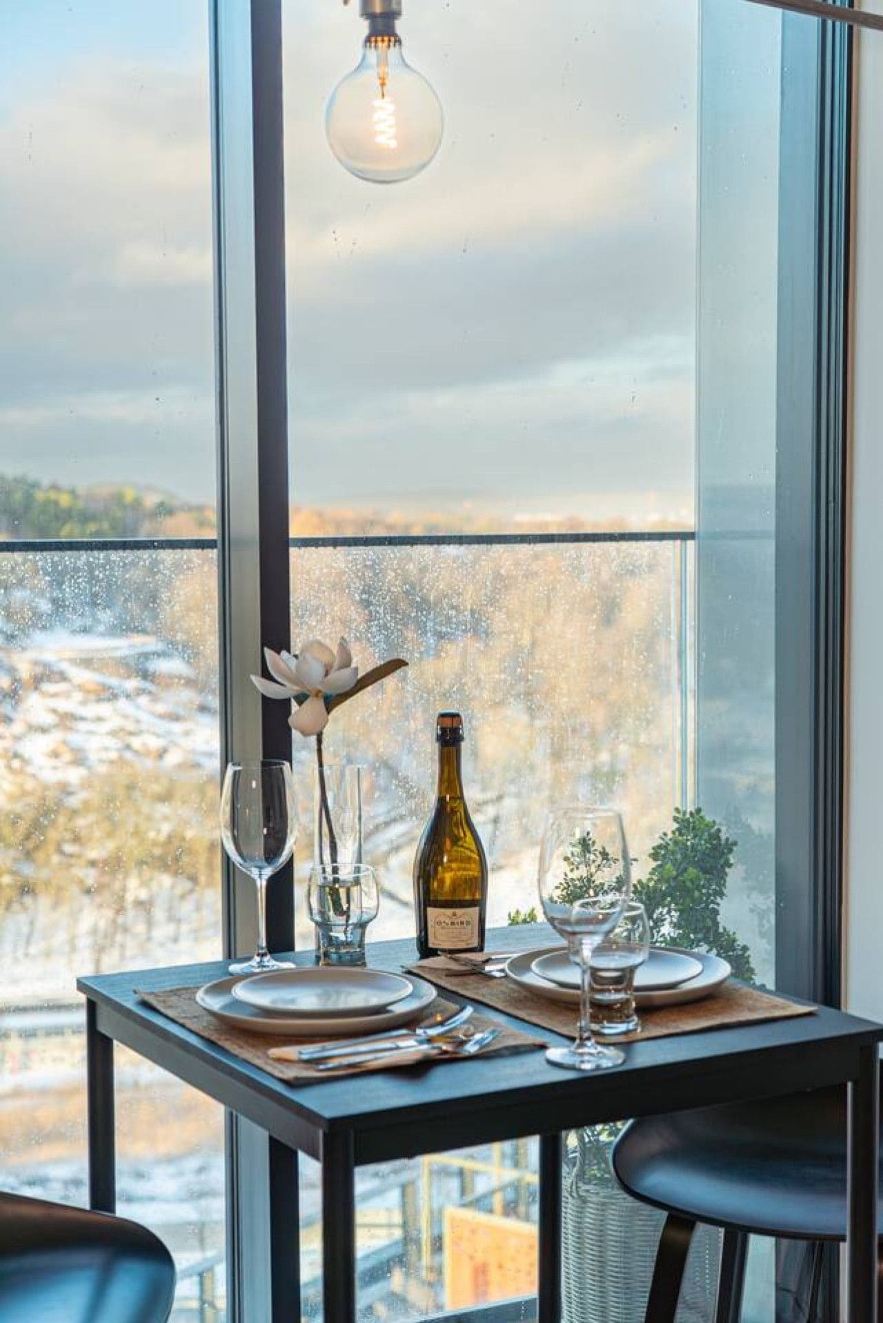 A dining table set with plates, glasses, a bottle, and a flower arrangement.