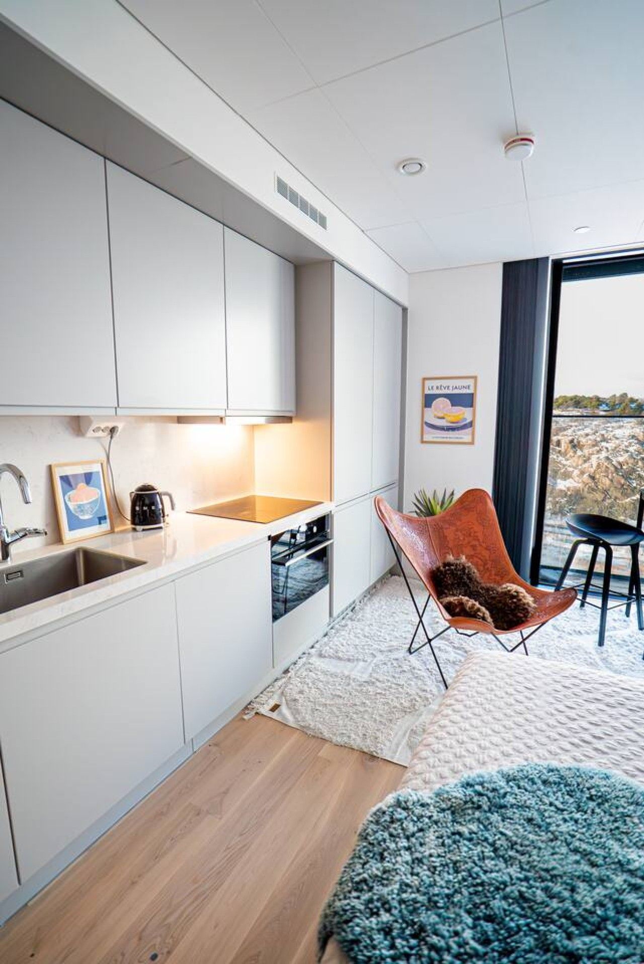 A modern kitchen with white cabinets, a sink, and a stove. There is a chair with a cushion and a rug on the floor.