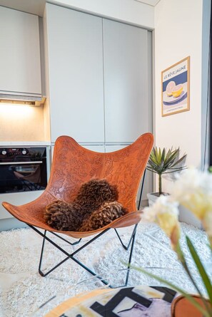 Une cuisine moderne avec des meubles blancs, une cuisinière et une chaise orange décorative dotée d’un coussin.