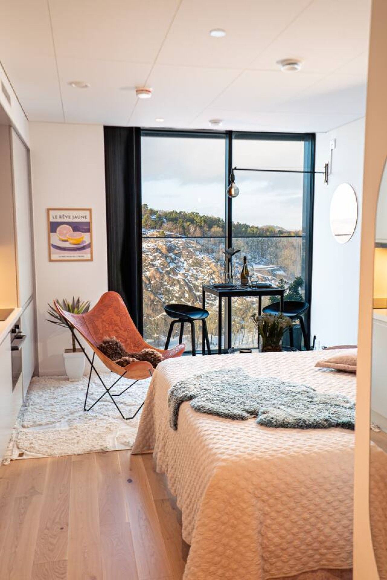 Ett sovrum med ett stort fönster, en stol, ett litet bord och en säng.