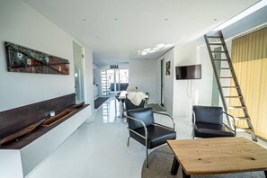 A modern living room with a sofa, chairs, a coffee table, a TV, and a ladder.