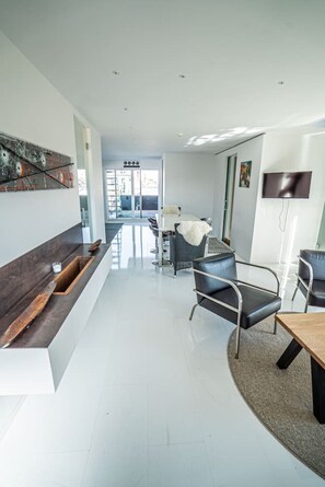 Ein modernes Interieur mit Küchenbereich, einem Esstisch mit Stühlen und einem an der Wand befestigten Fernseher.