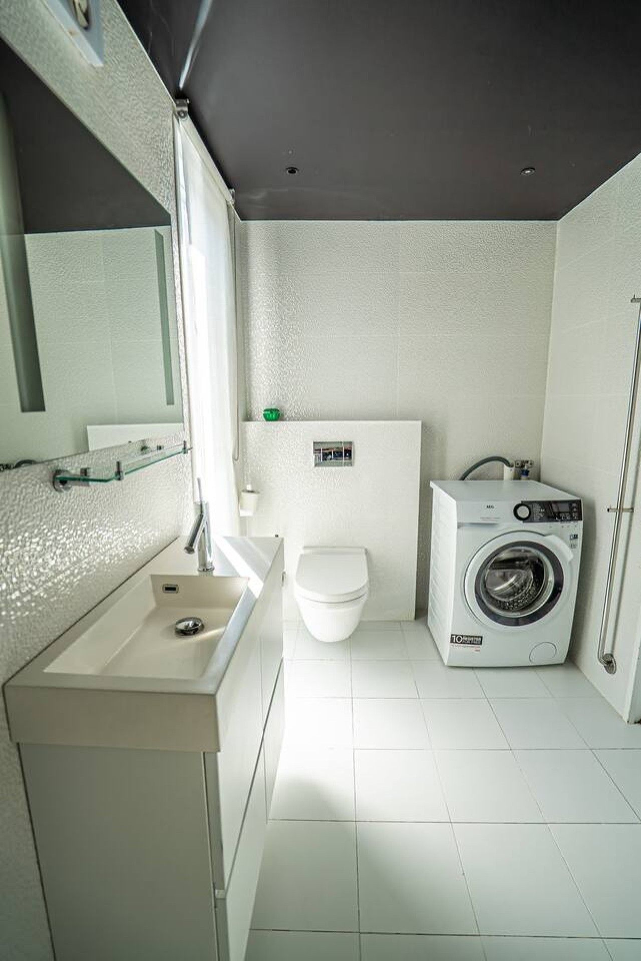 Et lille badeværelse med vask, toilet og vaskemaskine.