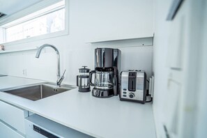 A modern kitchen with a sink, a coffee maker, a grinder, and a toaster.