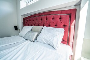 A bed with a red upholstered headboard, white bedding, and two pillows.