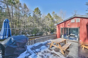 Ein rotes Gebäude mit Glastür und -fenstern, eine Holzterrasse und ein Picknicktisch, sowie ein blauer Sonnenschirm.