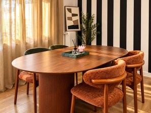 Une table de salle à manger ronde, entourée de six chaises rembourrées, un vase rempli de fleurs et, au mur, une œuvre d’art abstraite encadrée.
