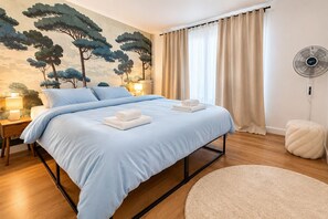 Ein Schlafzimmer mit einem Bett, einem Nachttisch, einem Wandventilator und einem runden Teppich.