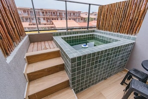 A hot tub area with tiled walls, wooden steps, and a view of buildings in the background. - New Listing (Ipojuca)