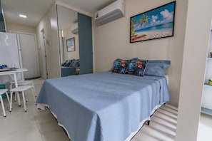 A bedroom with a bed, a desk, chairs, and a painting of a beach scene. - New Listing (Ipojuca)