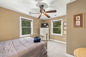 A bedroom with a bed, a ceiling fan, a television, and a window with a view of trees. - Mountain Lodge | 4BR + Game Room (Bartlett)