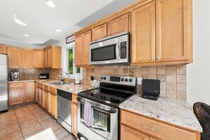 A modern kitchen with wooden cabinets, a stainless steel range, a microwave, and a dishwasher. - Mountain Lodge | 4BR + Game Room (Bartlett)