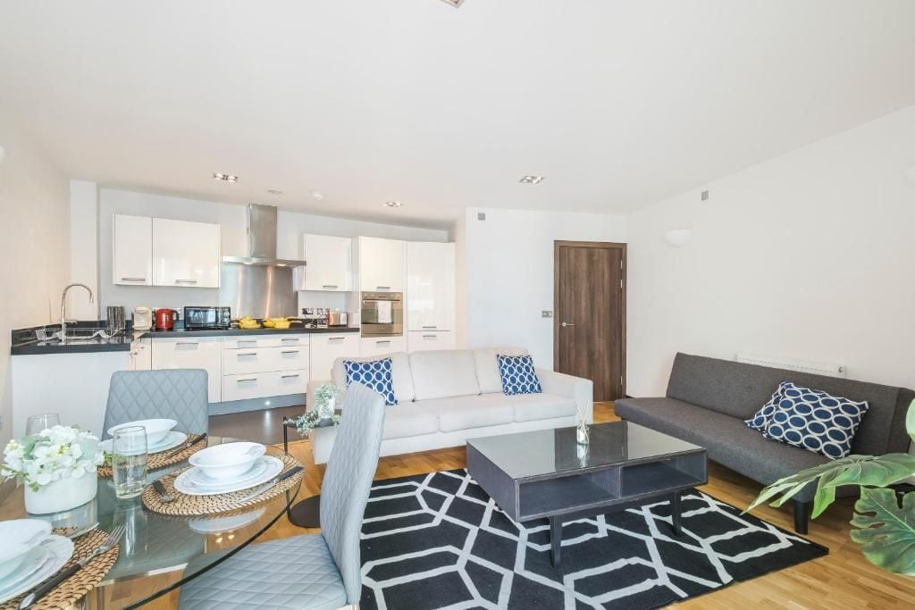A modern living space with a dining area, a sofa, and a kitchen in the background.