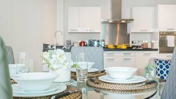 A modern kitchen with white cabinets, a stainless steel range hood, and a dining area with a glass table set with white plates and bowls.