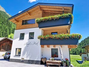 A two-story building with wooden balconies adorned with flower boxes, a sign reading 'Augl's Hof', and a heart-shaped stack of logs. - Augl´s Hof by Interhome (Ischgl)