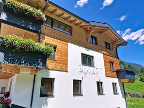 A multi-story building with wooden balconies, a sign reading 'Augel's Hof,' and a view of a green landscape. - Augl´s Hof by Interhome (Ischgl)