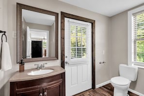 A bathroom with a white sink, dark wooden vanity, a large mirror, a white door with shutters, and a white toilet.