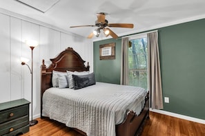 Une chambre à coucher avec un lit en bois, un ventilateur de plafond, une table de chevet et une fenêtre avec des rideaux.
