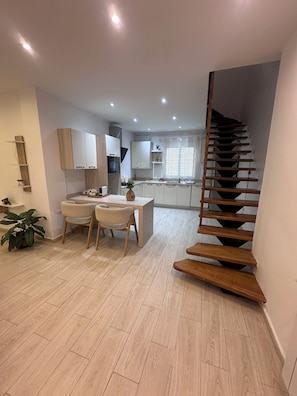 A modern kitchen with white cabinets, a dining area with a table and chairs, and a wooden staircase. - New Listing (Chéraga)