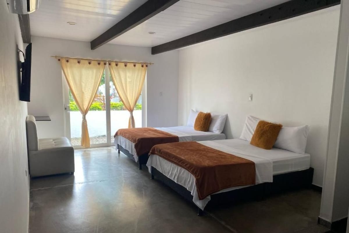 A hotel room with two beds, a small seating area, and a window with curtains.