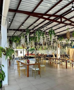 An indoor dining area with tables and chairs, a high ceiling with metal beams, and hanging plants. - Hotel Campestre Serrania de Manacacias (SAN MARTÍN)