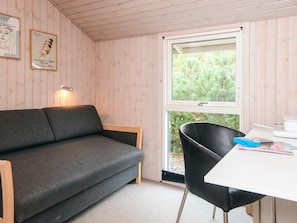 A room with a grey sofa, a black chair, a white table, and a window with a view of trees. - 6 Person Holiday Home in Juelsminde (Horsens)