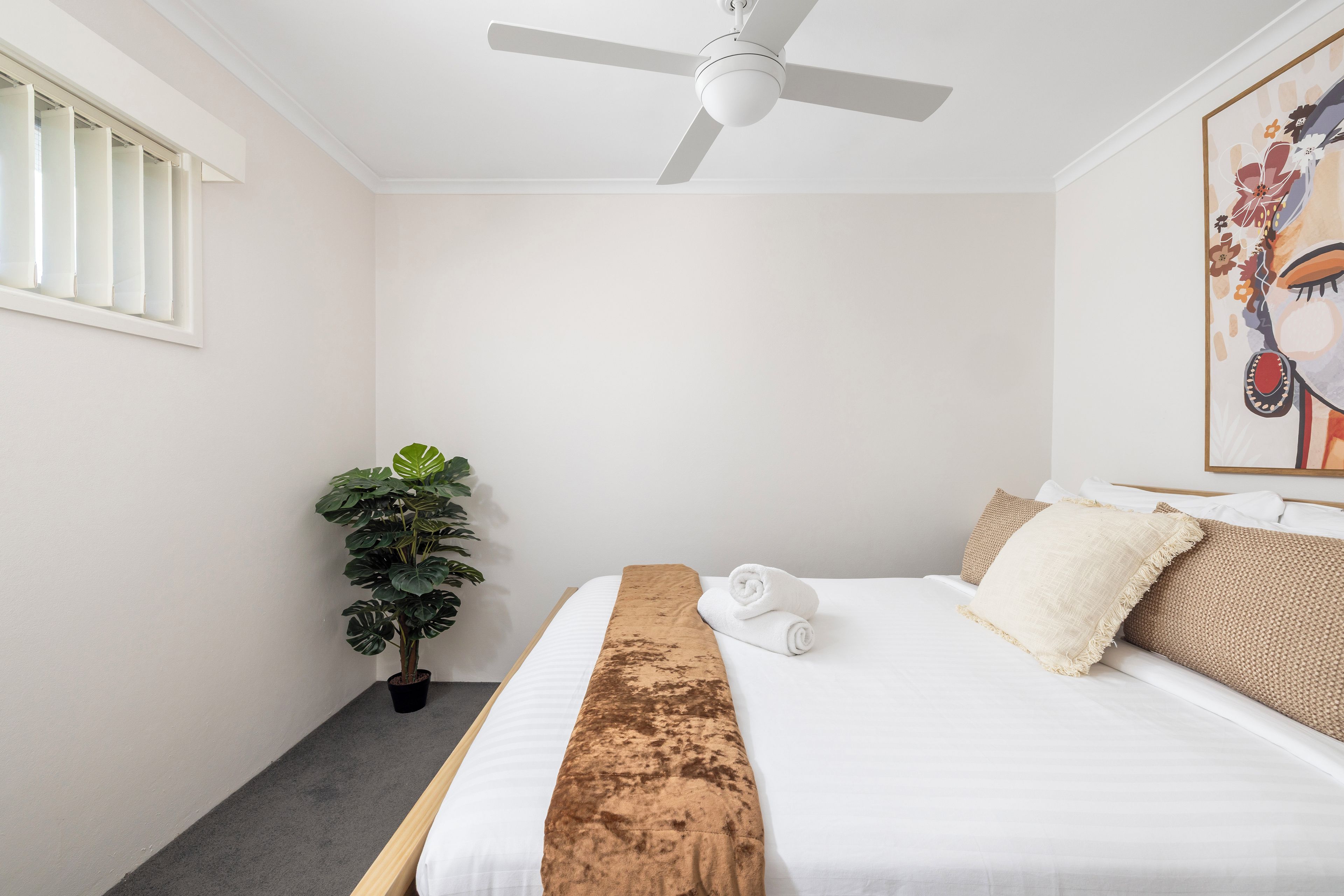 Een hotelkamer met een bed, een plafondventilator, een potplant en een schilderij aan de muur.