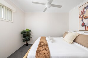 Een hotelkamer met een bed, een plafondventilator, een potplant en een schilderij aan de muur.