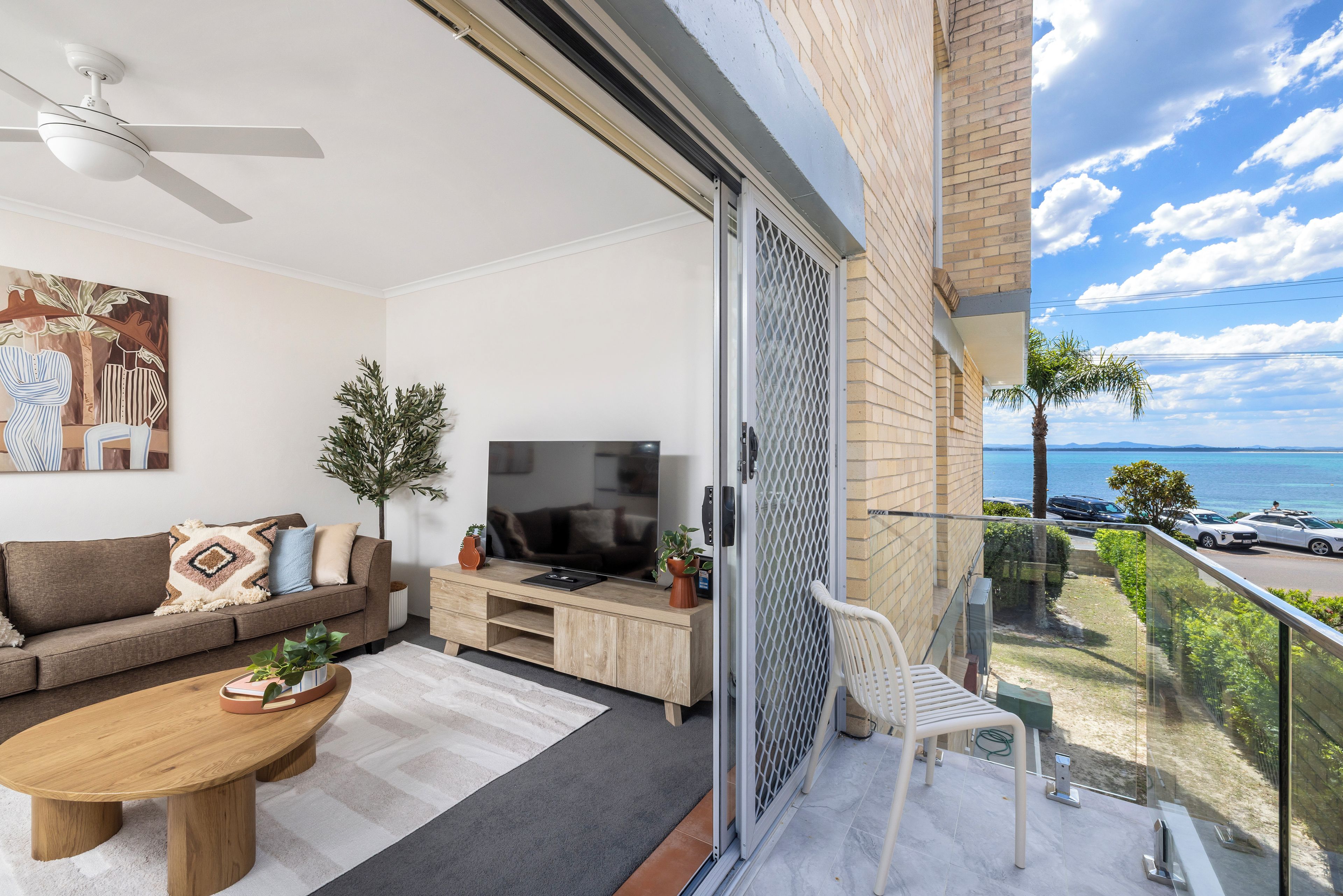 Een moderne woonkamer met een bank, salontafel, televisie en een balkon met uitzicht op zee.