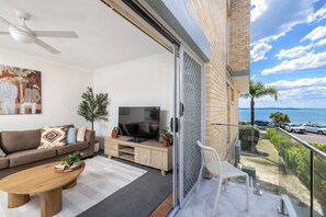 A modern living room with a sofa, coffee table, TV, and a balcony with a view of the sea. - Castaways Beachfront Shoal Bay (Shoal Bay)
