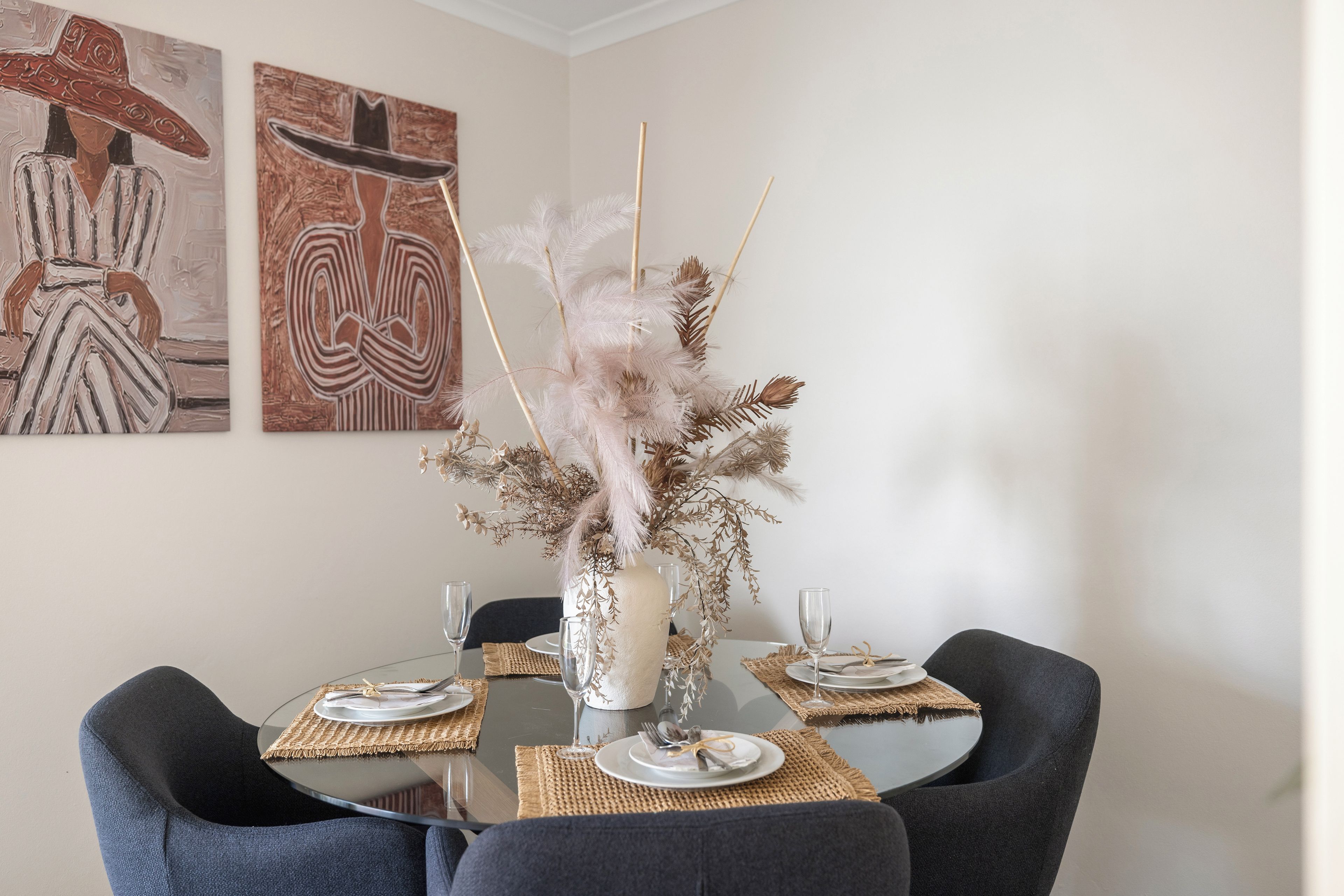 Een eettafel met een vaas droogbloemen, omringd door stoelen en placemats.