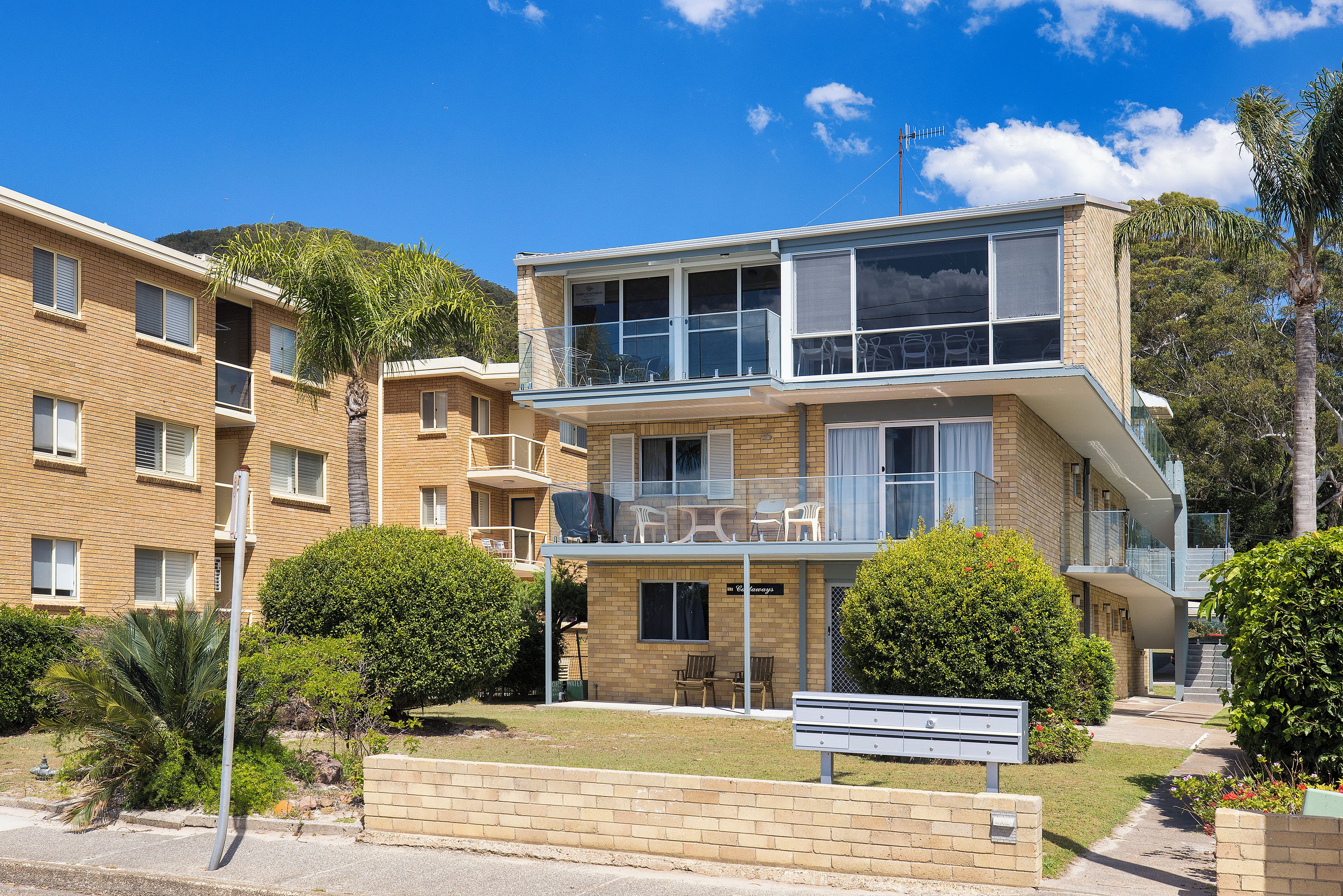 A multi-story residential building with a balcony, a small outdoor seating area, and a mailbox.