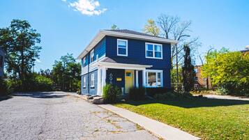 A two-story residential house with a front porch, a visible garage door, and a well-maintained lawn.