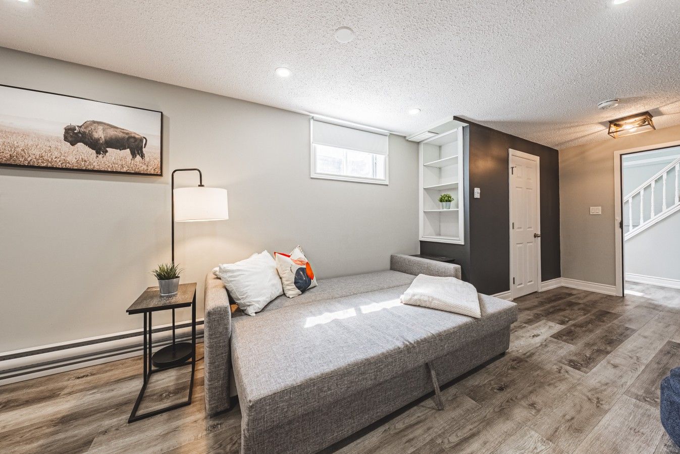 A modern living room with a gray sofa, a floor lamp, and a painting of a bison.