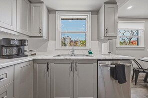 Une cuisine moderne équipée d’une machine à expresso intégrée, d’un évier et d’une fenêtre donnant sur des immeubles et des arbres.