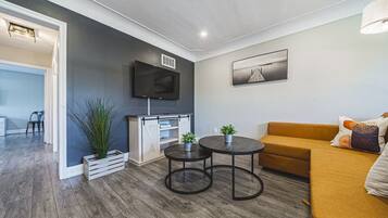 A modern living room with a sofa, a coffee table, a TV mounted on the wall, and a plant.