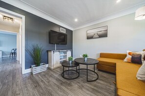 Un salon moderne avec un canapé, une table basse, un téléviseur fixé au mur et une plante.