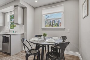 A modern kitchen with a dining area, white cabinetry, and a view through a window.