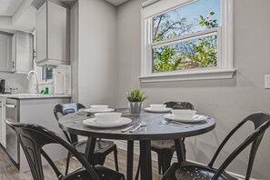 Un comedor con una mesa redonda dispuesta para cuatro personas, rodeada de sillas, una planta en maceta y un ventanal con vistas a árboles.