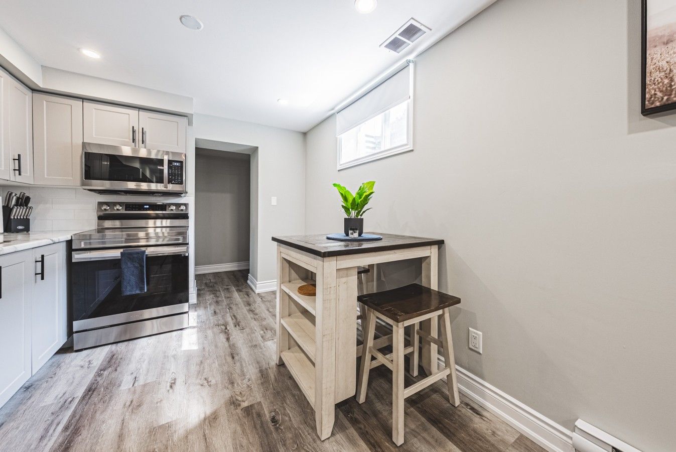 A compact kitchen with built-in appliances, a wooden stool, and a potted plant.