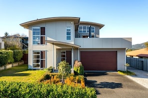 A modern two-story house with a curved roof, a garage, and a well-maintained front yard. - View from the Top - lake & mountain views! (Taupo)