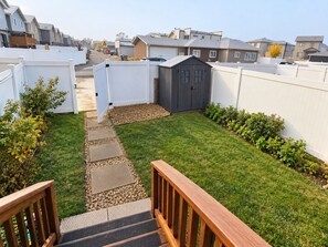 Ein Wohngrundstück mit Holzterrasse, kleiner Gartenhütte und gepflegtem Rasen.