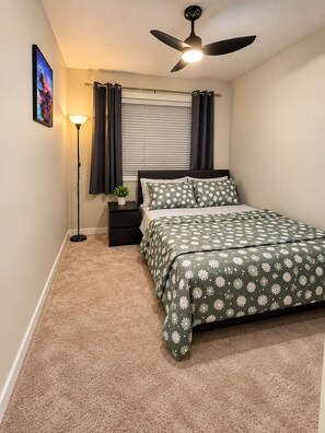 A bedroom with a bed, a ceiling fan, a nightstand, a lamp, and a window with curtains. - Modern 3BR/2.5BA Home | Free Parking, WiFi, Full Kitchen, Laundry & Deck (Regina)