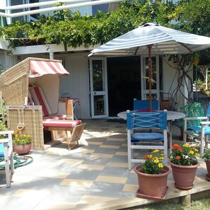 An outdoor patio with a checkered floor, wicker furniture, a striped umbrella, and potted plants. - Lovely 1-bedroom studio in Russell perfect for a relaxing getaway (Russell)